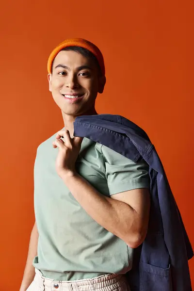A handsome Asian man in a green shirt is carrying a blue backpack against an orange background. — Stock Photo
