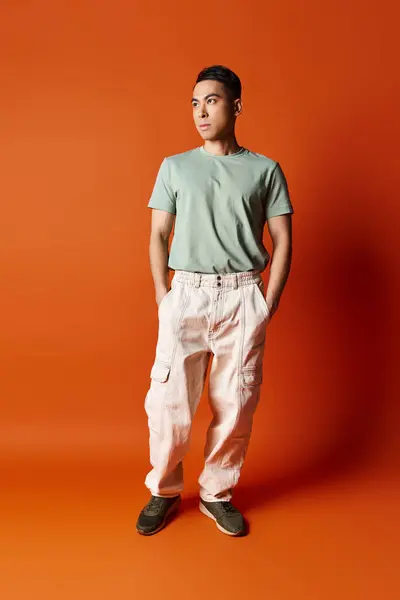 Красивий азіатський чоловік впевнено стоїть в стильному вбранні на тлі яскраво-помаранчевого фону в обстановці студії. — стокове фото