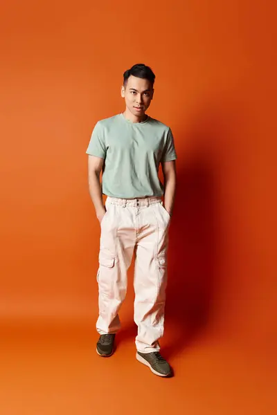 Красивий азіатський чоловік впевнено стоїть перед яскравою помаранчевою стіною, що дає відчуття стилю та індивідуальності. — стокове фото