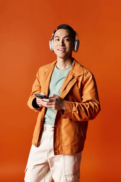 Un homme asiatique élégant portant des écouteurs, absorbé dans son téléphone portable. — Photo de stock