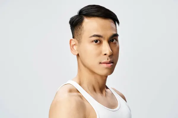 Un hombre asiático guapo en una camiseta sin mangas da una pose segura en un estudio gris. - foto de stock