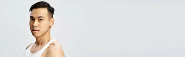 A handsome Asian man in a white tank top strikes a confident pose in a grey studio setting. — Stock Photo