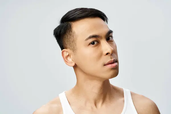 A handsome Asian man in a tank top gazes thoughtfully off to the side in a grey studio setting. — Stock Photo