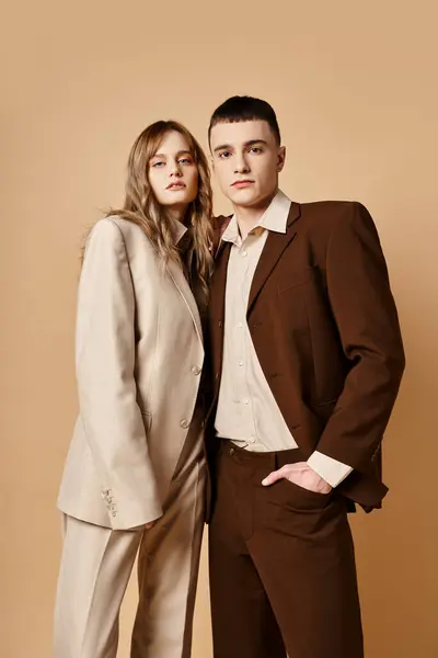Verführerisch elegantes Paar in Debonair-Anzügen posiert zusammen und blickt vor pastellfarbener Kulisse in die Kamera — Stockfoto