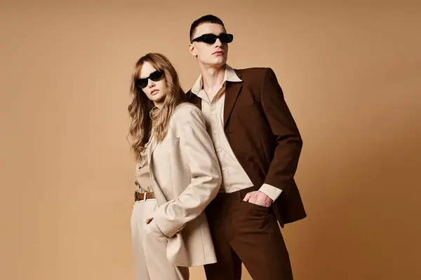 Appealing elegant couple in chic seasonal suits with stylish sunglasses posing on pastel background — Stock Photo