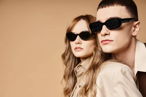 Attraktives elegantes Paar in schicken saisonalen Anzügen mit stylischer Sonnenbrille posiert auf pastellfarbenem Hintergrund — Stockfoto
