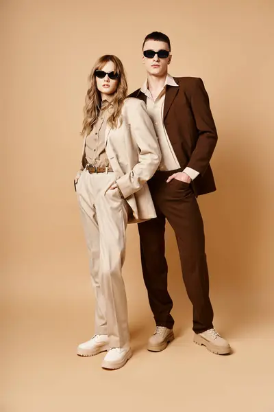Atraente casal elegante em ternos sazonais chiques com óculos de sol elegantes posando no fundo pastel — Fotografia de Stock