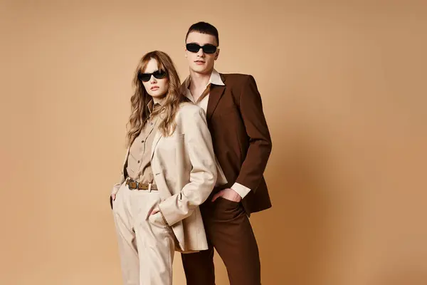 Очаровательная элегантная пара в шикарных сезонных костюмах в стильных солнцезащитных очках, позирующих на пастельном фоне — стоковое фото