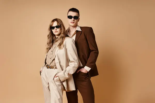 Séduisant couple élégant en costumes de saison chic avec des lunettes de soleil élégantes posant sur fond pastel — Photo de stock