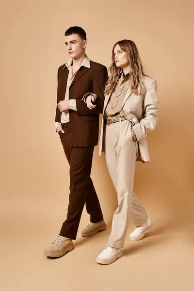 Sofisticada pareja joven en trajes elegantes posando juntos y mirando hacia otro lado sobre fondo pastel - foto de stock