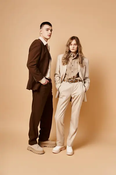 Loving elegant boyfriend and girlfriend in chic suits looking at camera on pastel background — Stock Photo