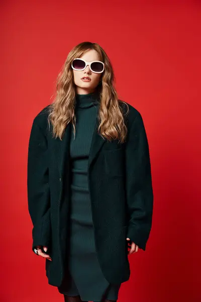 Belle femme à la mode en tenue élégante avec des lunettes de soleil posant sur fond rouge vibrant — Photo de stock