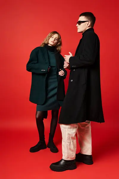 Attraktive langhaarige Frau im eleganten Mantel, die in die Kamera neben ihrem Freund mit Sonnenbrille blickt — Stockfoto