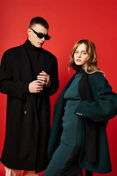 Привлекательная длинноволосая женщина в элегантном пальто смотрит в камеру рядом со своим парнем в солнечных очках — стоковое фото