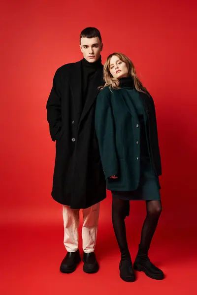 Atractivo pareja amorosa en sofisticados abrigos mirando a la cámara en rojo vibrante fondo - foto de stock