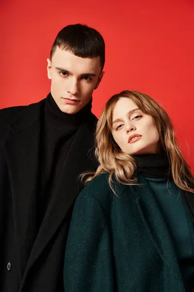 Atractivo pareja amorosa en sofisticados abrigos mirando a la cámara en rojo vibrante fondo - foto de stock