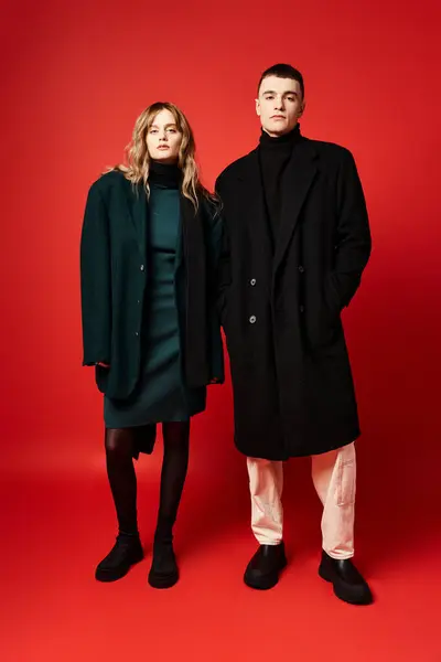 Alluring loving couple in sophisticated chic coats looking at camera on red vibrant background — Stock Photo