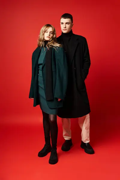Beautiful woman in coat looking at camera and posing lovingly with her boyfriend on red backdrop — Stock Photo