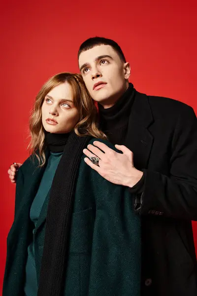Hermosa pareja elegante en elegantes abrigos posando juntos y mirando hacia otro lado en el vibrante telón de fondo - foto de stock