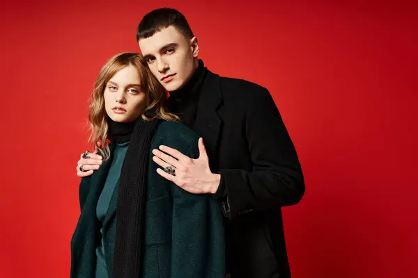 Alluring loving couple in sophisticated chic coats looking at camera on red vibrant background — Stock Photo