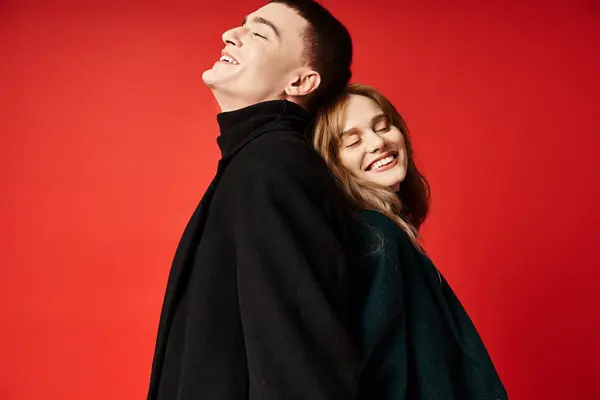 Fröhliches Liebespaar in stylischen Mänteln, glücklich lächelnd mit geschlossenen Augen vor rotem Hintergrund — Stockfoto