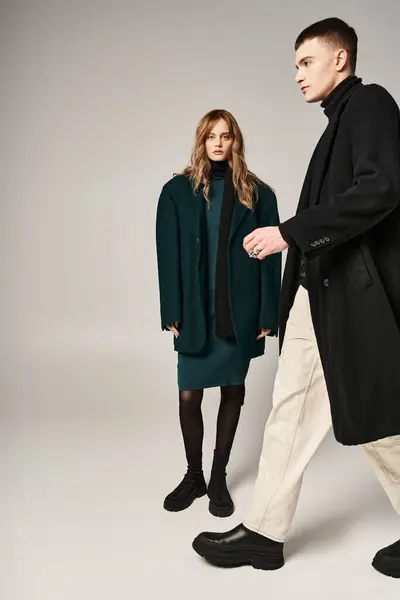 Good looking trendy boyfriend and girlfriend in coats posing lovingly together on gray backdrop — Stock Photo