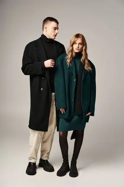 Beau copain élégant et petite amie en manteaux posant ensemble avec amour sur fond gris — Photo de stock
