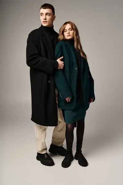 Gut aussehender stylischer Freund und Freundin in Mänteln posieren liebevoll zusammen vor grauem Hintergrund — Stockfoto