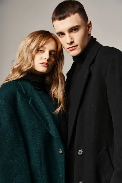 Сложная пара в стильных пальто позируют вместе на сером фоне и смотрят в камеру — стоковое фото