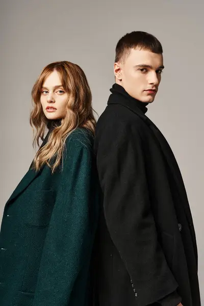 Appealing trendy boyfriend and girlfriend in coats posing and looking at camera on gray backdrop — Stock Photo
