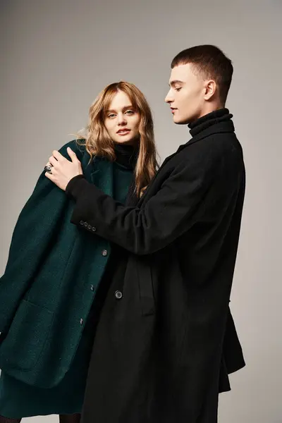 Atractivo hombre de abrigo posando amorosamente junto a su hermosa novia que mira a la cámara - foto de stock