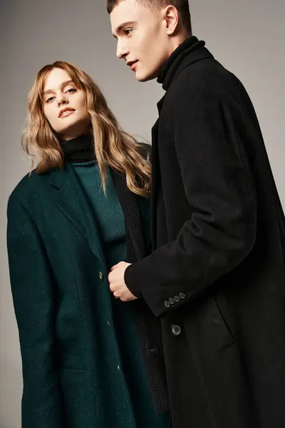 Привлекательный мужчина в пальто с любовью позирует рядом со своей красивой девушкой, которая смотрит в камеру — стоковое фото