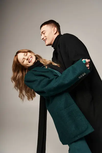 Joyeux couple attrayant dans des manteaux élégants souriant joyeusement et ayant du temps de qualité sur fond gris — Photo de stock