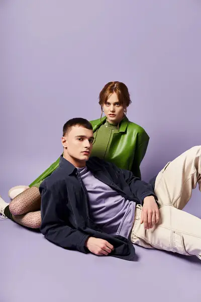 Хорошо одетые пары в ярких одеждах сидят на полу и смотрят на камеру на фиолетовом фоне — стоковое фото