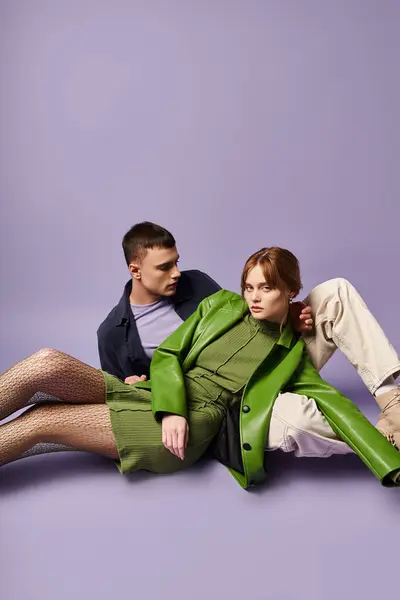 Hermosa mujer con estilo en chaqueta verde sentado en el suelo con su novio y mirando a la cámara - foto de stock