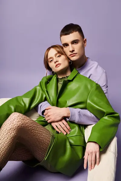 Attraente coppia in abiti vibranti seduto sul pavimento e guardando la fotocamera su sfondo viola — Foto stock