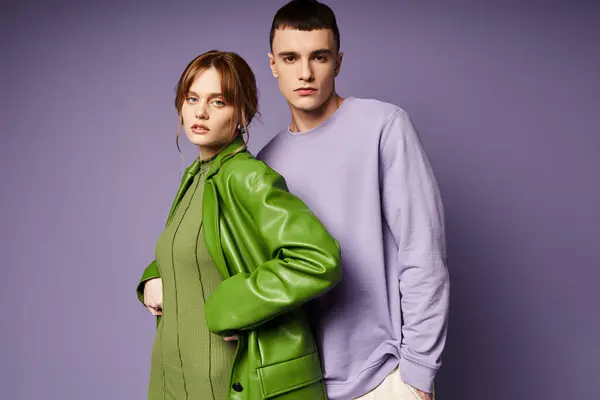 Couple à la mode dans des vêtements vibrants posant ensemble sur fond violet et regardant la caméra — Stock Photo