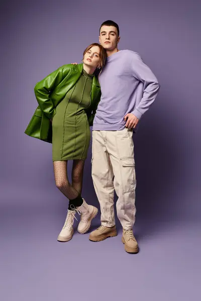 Casal sofisticado em roupas vibrantes posando juntos no fundo roxo e olhando para a câmera — Fotografia de Stock