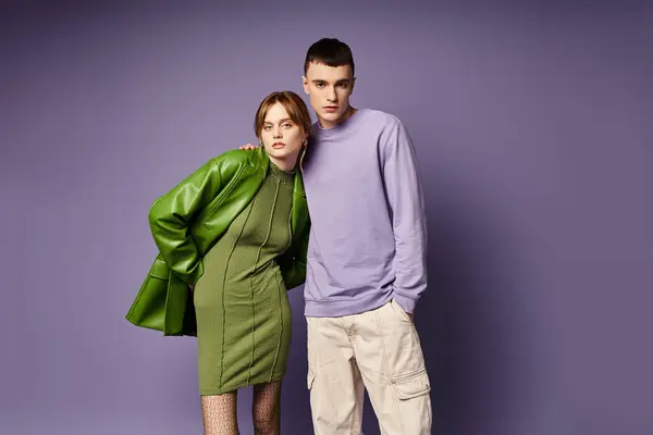 Well dressed couple in vibrant clothes posing together on purple background and looking at camera — Stock Photo