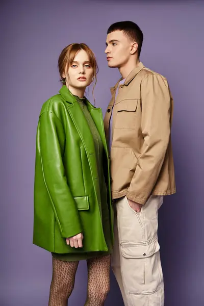 Mulher atraente em casaco verde olhando para a câmera perto de seu namorado amoroso em pano de fundo roxo — Fotografia de Stock