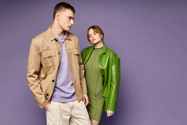 Заманчивая женщина в зеленой куртке смотрит в камеру рядом со своим любящим парнем на фиолетовом фоне — стоковое фото