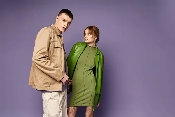 Appealing young woman in green jacket looking lovingly at her handsome boyfriend on purple backdrop — Stock Photo