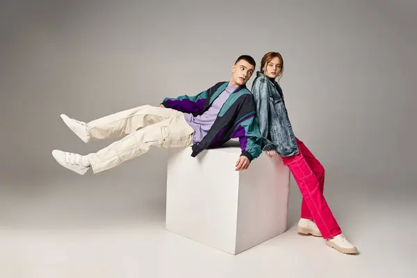 Elegant woman in fashionable bomber looking at camera next to her handsome boyfriend on white cube — Stock Photo
