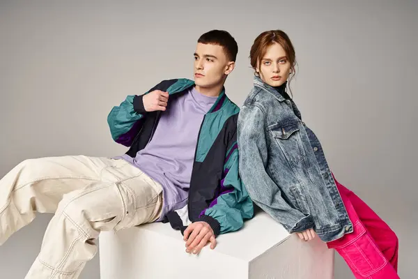 Beautiful woman in fashionable bomber looking at camera next to her handsome boyfriend on white cube — Stock Photo