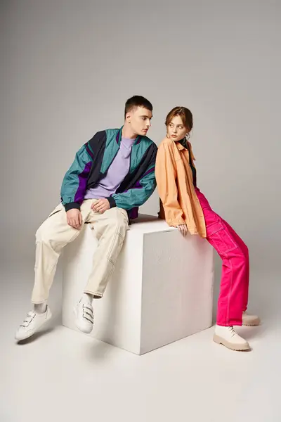 Young appealing couple in vibrant trendy bombers looking at each other lovingly on white cube — Stock Photo