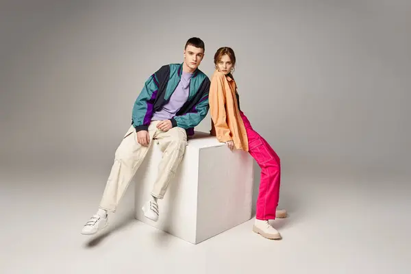 Loving fashionable couple in vivid stylish bombers looking at camera on gray backdrop on white cube — Stock Photo