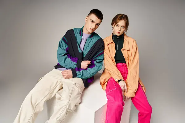 Loving fashionable couple in vivid stylish bombers looking at camera on gray backdrop on white cube — Stock Photo
