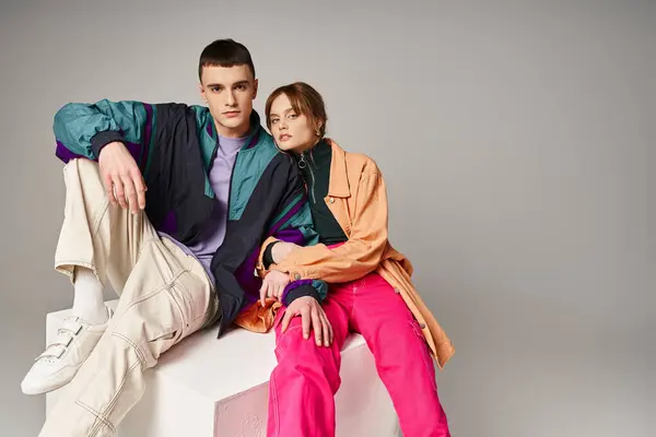 Caring fashionable couple in vivid stylish bombers looking at camera on gray backdrop on white cube — Stock Photo