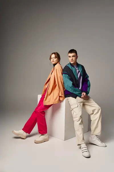 Caring fashionable couple in vivid stylish bombers looking at camera on gray backdrop on white cube — Stock Photo