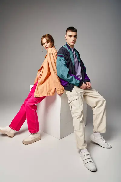 Caring appealing couple in vivid stylish bombers looking at camera on gray backdrop on white cube — Stock Photo